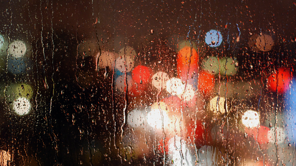 Rain streaking down a window with city lights blurred in the dark background.